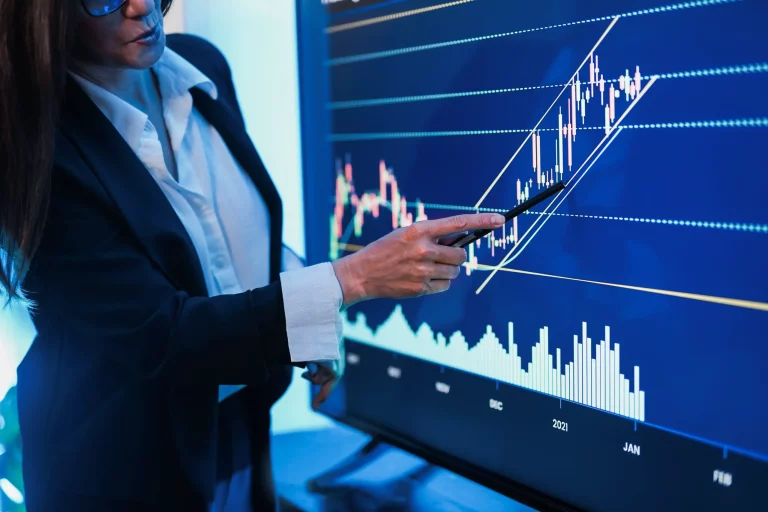 Professional woman presenting trading strategies to colleagues inside a modern office.