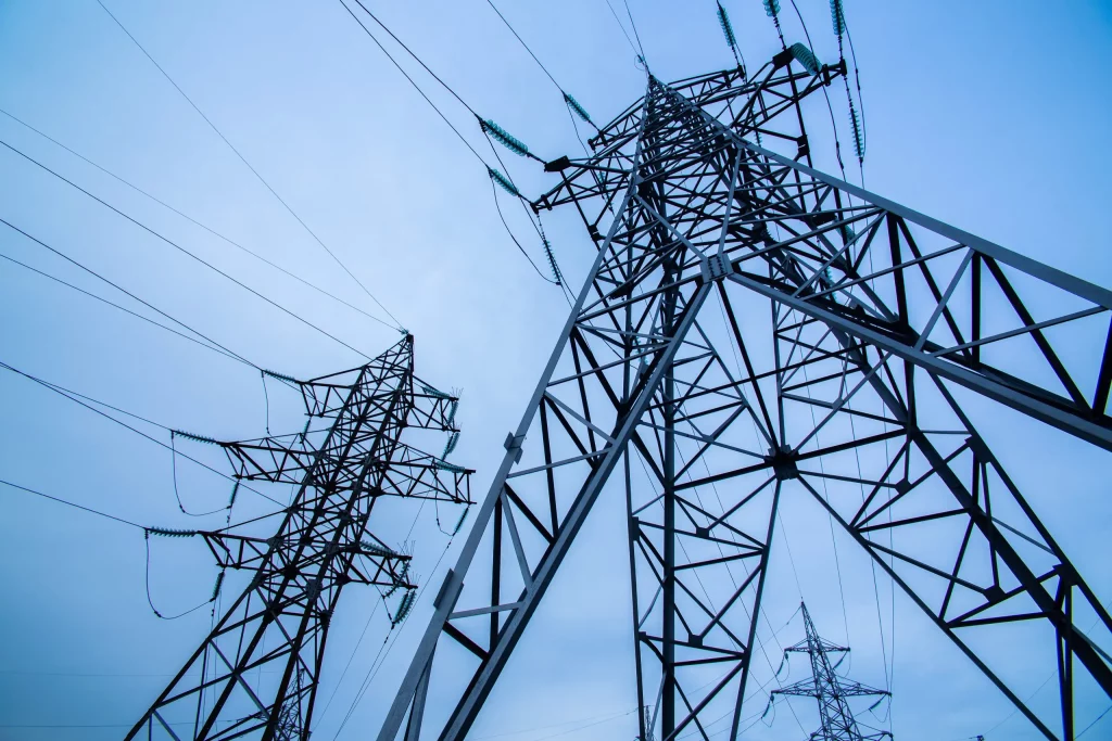 High-voltage electricity pylons silhouetted against a bright blue sky, symbolizing power supply and infrastructure.