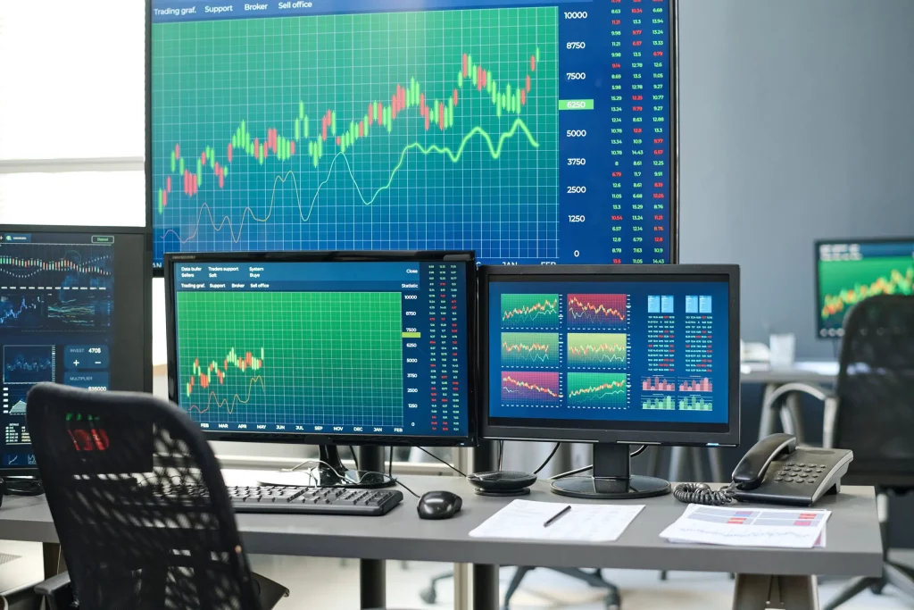 Trading office with multiple monitors displaying stock charts, graphs, and live market statistics.