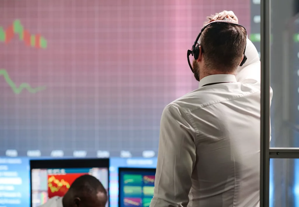 Person analyzing live stock trading data across several computer screens in a modern office.